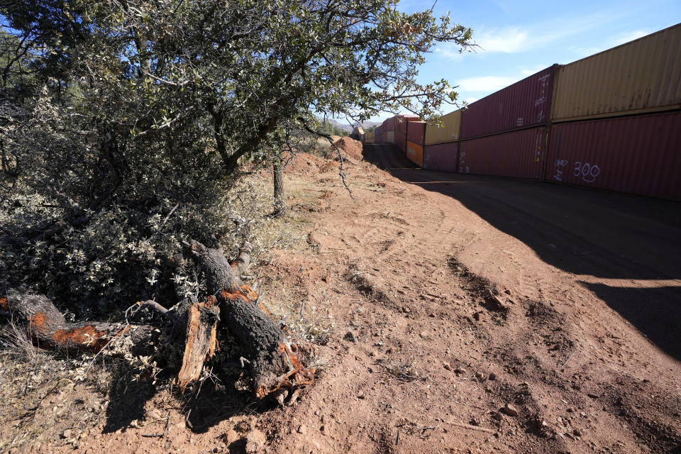 Downed trees are pushed aside on top of piles of moved dirt along the border where shipping containers create a wall between the United States and Mexico in San Rafael Valley, Ariz., Thursday, Dec. 8, 2022. Work crews are steadily erecting hundreds of double-stacked shipping containers along the rugged east end of Arizona’s boundary with Mexico as Republican Gov. Doug Ducey makes a bold show of border enforcement even as he prepares to step aside next month for Democratic Governor-elect Katie Hobbs. (AP Photo/Ross D. Franklin)