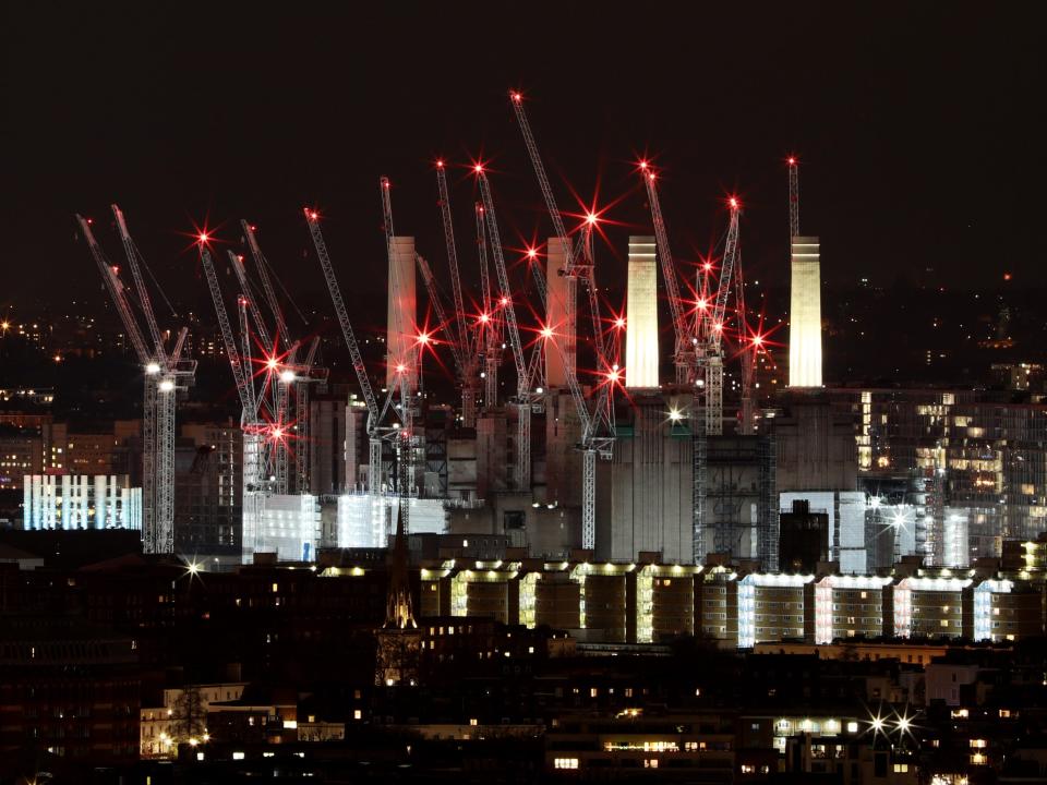 A photo of a power station with four chimneys towering above buildings in London, surrounded by cranes.