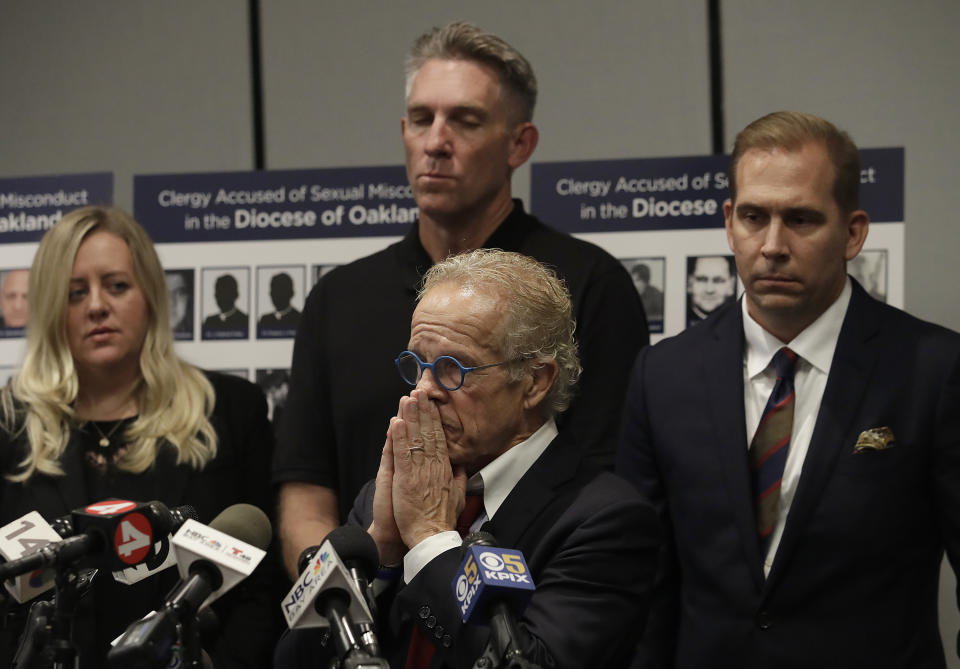 Attorney Jeff Anderson, bottom, listens to questions in front of Tom Emens, center rear, and attorney Mike Reck, right, at a news conference in San Francisco, Tuesday, Oct. 23, 2018. A law firm suing California bishops for the records of priests accused of sexual abuse has compiled a report of clergy in the San Francisco Bay Area it says are accused of misconduct. (AP Photo/Jeff Chiu)