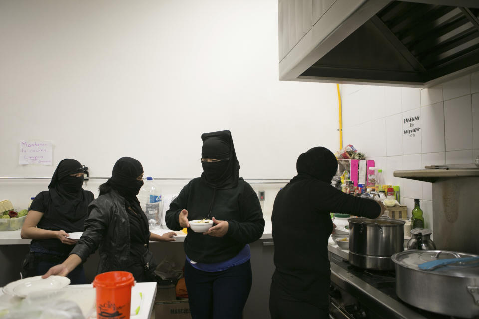 Women’s rights activists who say they cover their faces because they fear for their safety, serve dinner in the kitchen at the offices of the Mexican Human Rights Commission (CNDH), which they have been occupying for almost three months in Mexico City, Monday, Nov. 16, 2020. Feminist activists are occupying the CNDH to demand justice for the victims of sexual abuse, femicide, and other gender violence, and have opened it as a refuge to victims of sexual violence, where some mothers have brought their children to live while the government either failed to solve or even investigate the rapes of their daughters. (AP Photo/Ginnette Riquelme)
