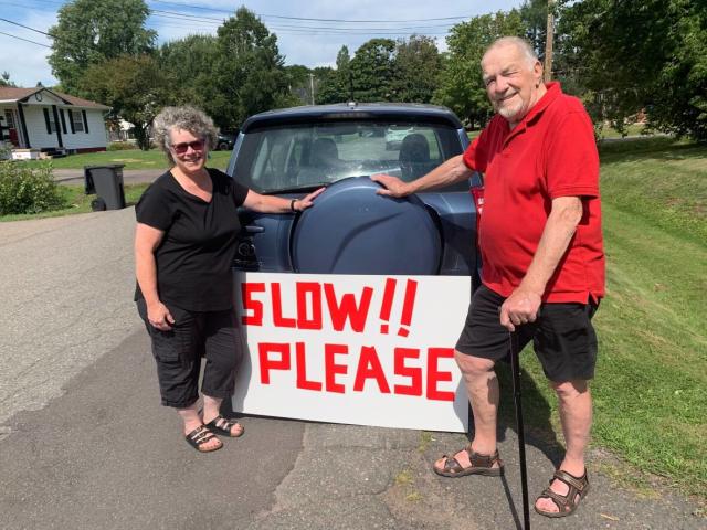John and Susan Whitaker made a sign in hopes of getting traffic to slow down.  Susan said it didn't make sense to have traffic directed down their street. Detour arrows were moved after complaints, but there is still increased traffic.  (Laura Meader/CBC - image credit)