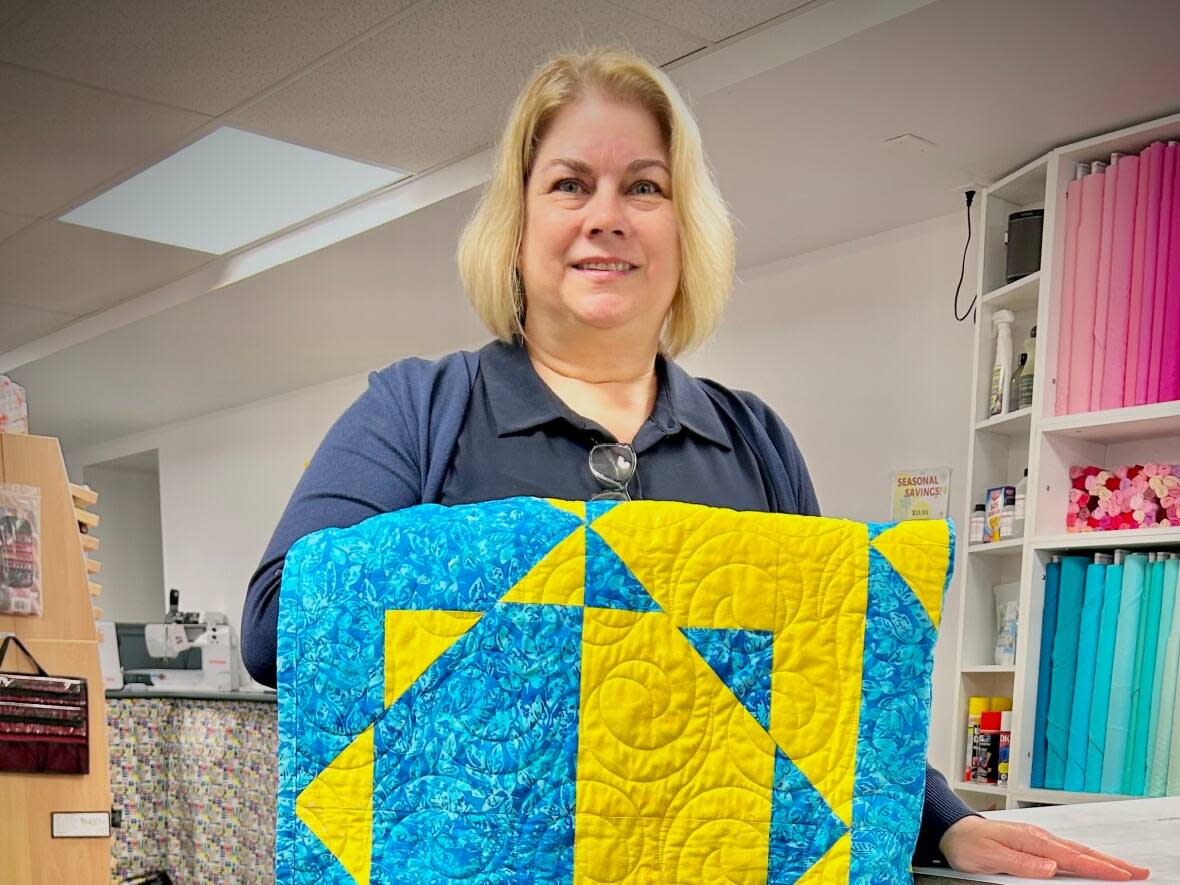 Volunteer Colleen McConnell holds a quilt made with the colours of the Ukrainian flag. (Amanda Gear/CBC - image credit)