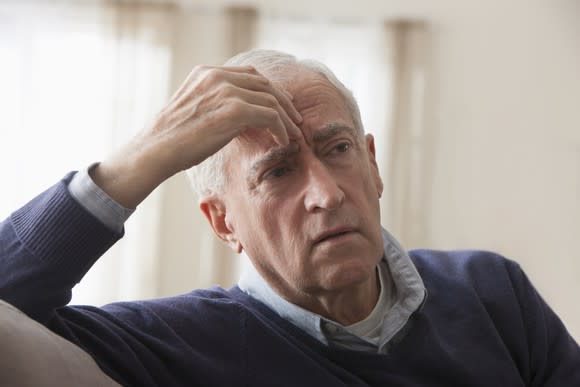 A worried elderly man with his hand on his forehead.