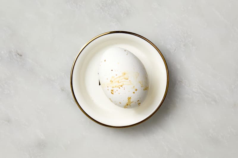 overhead shot of a boiled egg with the shell on, on a white plate with a gold rim.