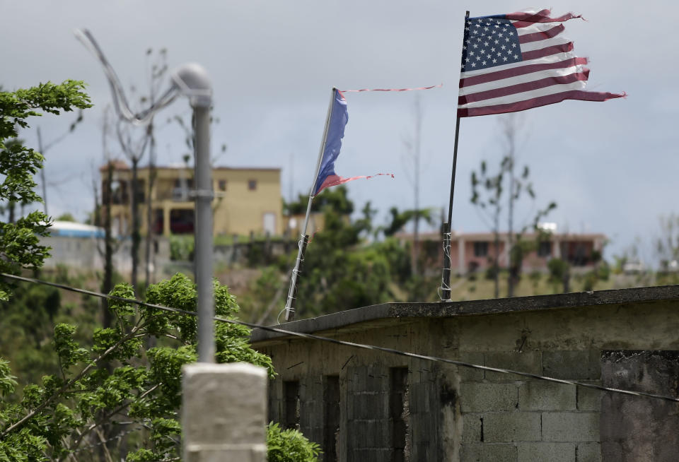 FILE - In this May 16, 2018 file photo, deteriorated U.S. and Puerto Rico flags fly on a roof eight months after the passing of Hurricane Maria in the Barrio Jacana Piedra Blanca area of Yabucoa, a town where power was knocked out by the storm. Though President Donald Trump continued one year after the storm to assert that his administration's efforts in Puerto Rico were "incredibly successful," both the local and federal governments have been heavily criticized for inadequate planning and post-storm response. (AP Photo/Carlos Giusti, File)