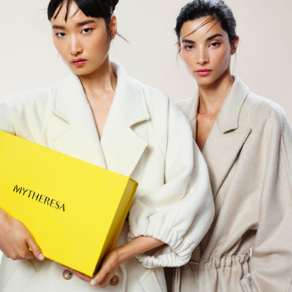  Two young woman in neutral wool coats with one holding yellow Mytheresa box. 