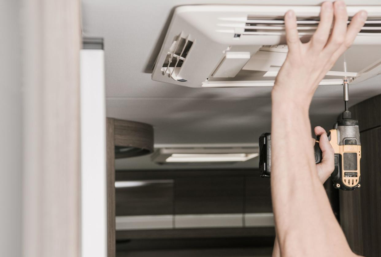 RV Recreational Vehicle Air Conditioner Installation. Caucasian Technician Installing Cooling Unit Inside Modern Camper Van.