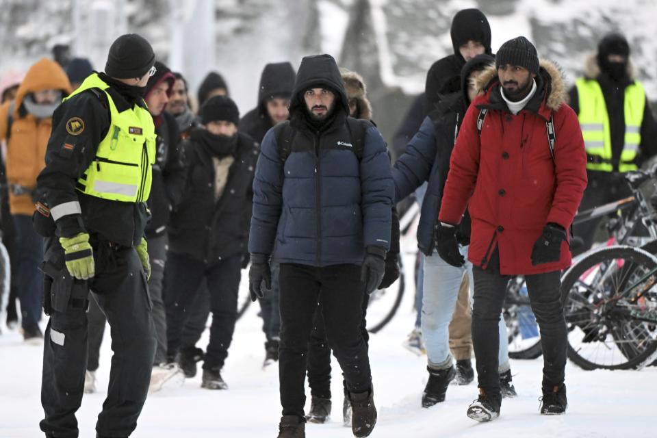 Finnish Border Guards escort migrants at the international border crossing between Finland and Russia, in Salla, Finland, Thursday, Nov. 23, 2023. (Jussi Nukari/Lehtikuva via AP)