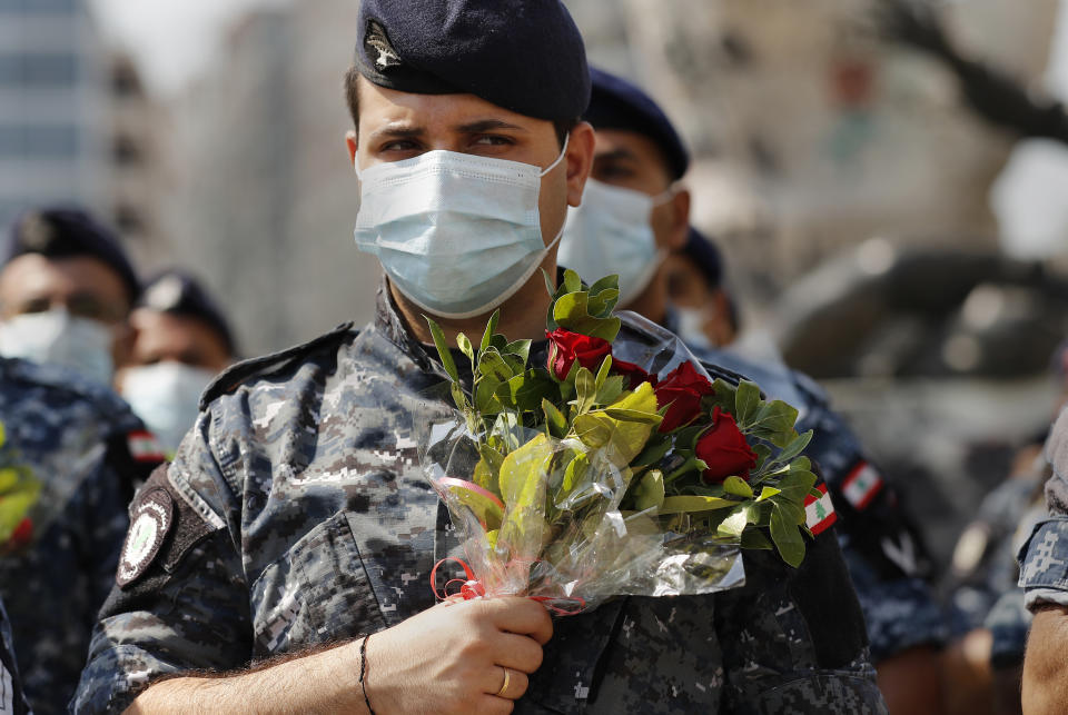 Police hold flowers to mark the first anniversary of Beirut's massive 2020 seaport blast in Beirut, Lebanon, Wednesday, Aug. 4, 2021. Lebanon is marking one year since the horrific explosion at Beirut port. The grim anniversary Wednesday comes amid an unprecedented economic and financial meltdown and a political stalemate that has kept the country without a functioning government for a full year. (AP Photo/Hussein Malla)