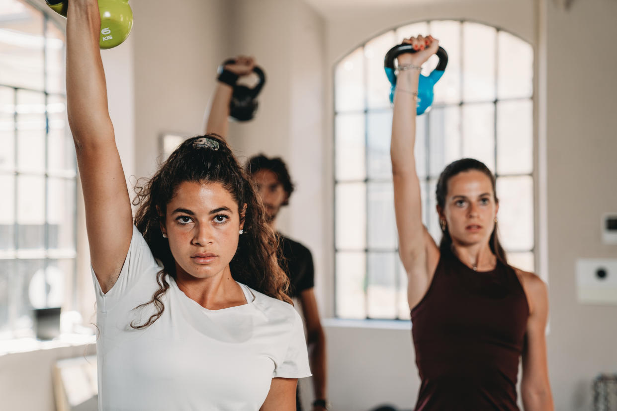 Three people at the health club are training together. They are using kettlebells.