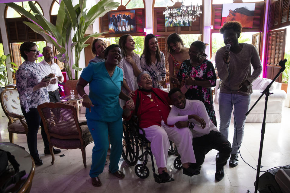 Familiares y empleados domésticos rodean a Huguette Mevs cantando canciones tradicionales para celebrar su 92do cumpleaños, en su casa en Puerto Príncipe, Haití, el 3 de octubre de 2021. Huguette Mevs forma parte de una de las familias más ricas de Haiti: su hija Youri es la propietaria de Shodecosa, el parque empresarial más grande del país, donde se almacena el 93% de la comida importada por la nación caribeña. (AP Foto/Rodrigo Abd)