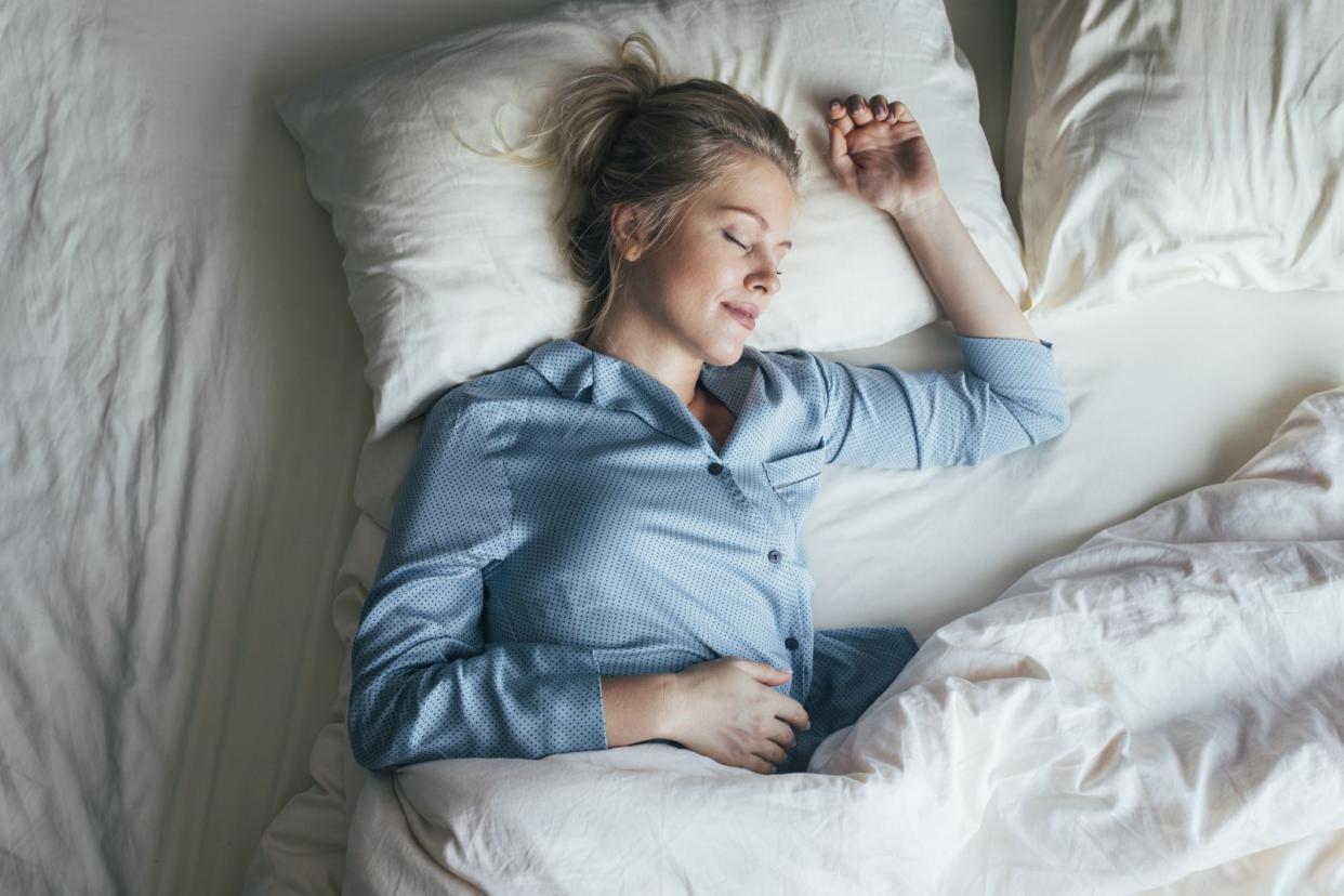 Beautiful happy Caucasian woman in blue pyjamas sleeping on a king-size bed.