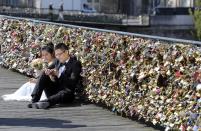 A newly wed couple rest on the Pont des Arts in Paris, Wednesday April 16, 2014. A recent fad among travellers of hitching padlocks on bridges and at tourist attractions worldwide to symbolically immortalize their amorous attraction has swept up this reputed City of Love more than most. Now, two American-born women who live in Paris say they've had enough, launching a petition drive to try to get mostly laissez-faire city officials to step in and do something about what they call an unbearable eyesore in a majestic municipality. (AP Photo/Remy de la Mauviniere)