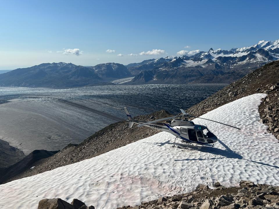 a helicopter on a snow back in front of the Alaskan mountains