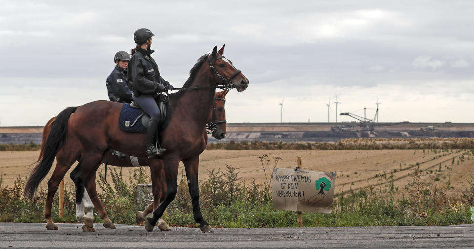 Police officers on horses secure the Garzweiler surface coal mine, passing a sign reading 'climate activism is not a crime' near Keyenberg, Germany, Friday, Sept. 25, 2020. Several groups like 'Friday for Future' or 'Ende Gelaende' started actions for climate justice in the coming days throughout Germany. The movement demands that the German government phase out coal by 2030 and make Germany carbon neutral by 2035. (AP Photo/Martin Meissner)