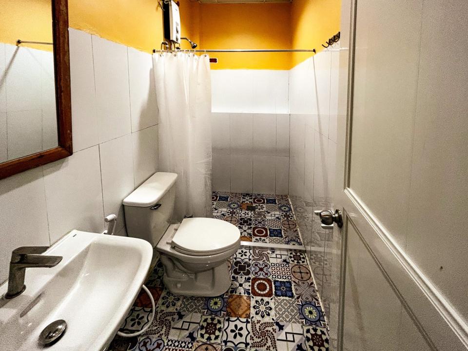 A small bathroom with a shower, a toilet, a sink with a bathroom mirror, and a tiled floor.