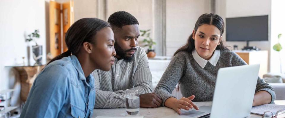 Financial planner going over savings plans on a laptop with a young couple at a table in their living room at home