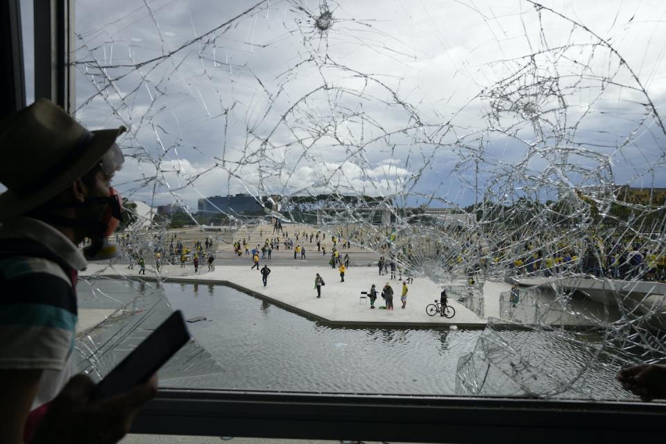 A supporter of Jair Bolsonaro looks out from a shattered window of the Planalto Palace after he and his fellow protesters stormed it in Brasilia, Brazil, in January 2023. (AP Photo/Eraldo Peres)