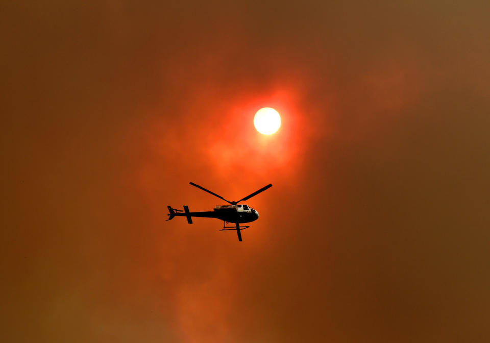 A spotter helicopter flies through thick bushfire smoke in Nana Glen, near Coffs Harbour, Tuesday, November 12, 2019. There are more than 50 fires burning around the state, with about half of those uncontained. (AAP Image/Dan Peled) NO ARCHIVING