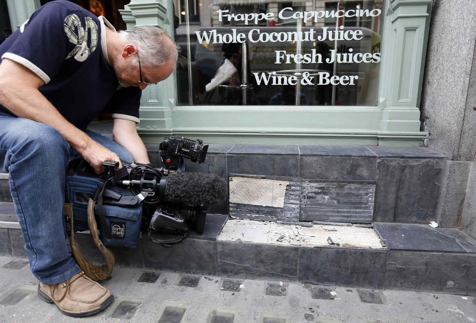 A camera man films broken slates outside a cafe in London