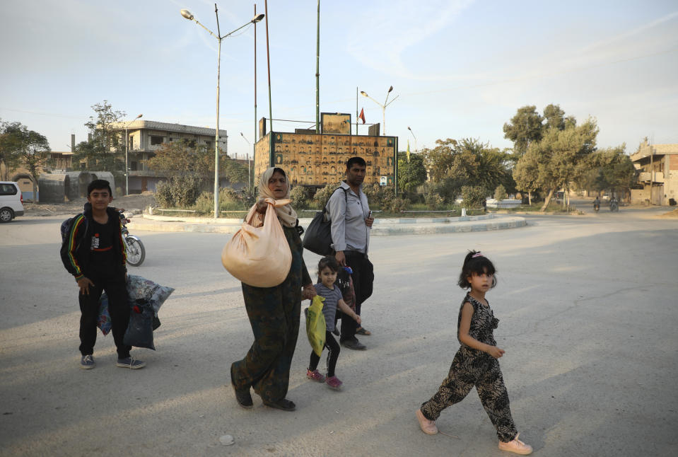 In this photo provided by Rojava Media Center, a pro-Kurdish media group, Syrians carry their belongings, as they flee Ras al Ayn, in northeast Syria, Wednesday, Oct. 9, 2019. (Rojava Media Center via AP)