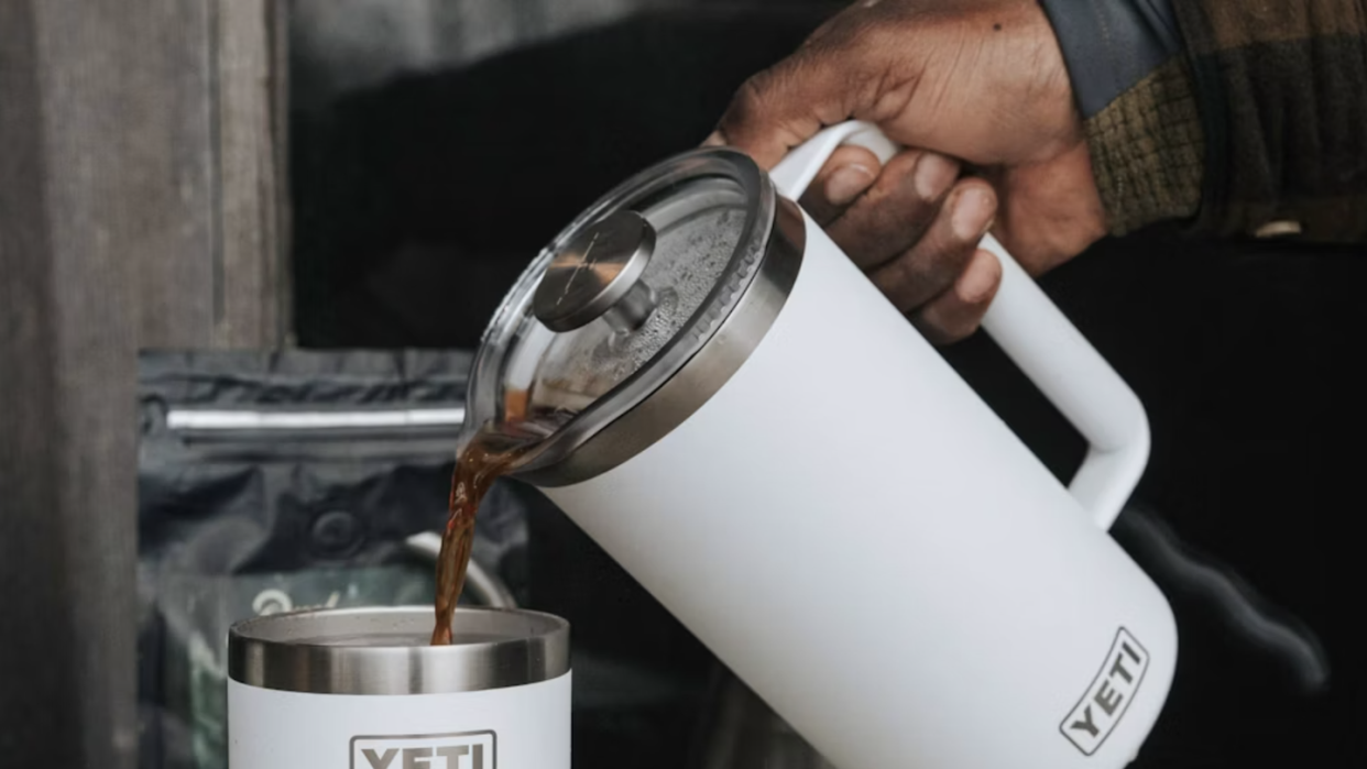 a hand pouring coffee out of a white yeti stainless steel french press