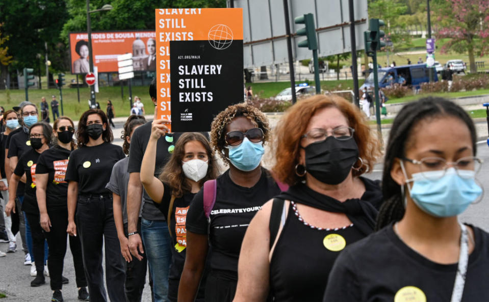 People wearing masks and holding signs that read "Slavery Still Exists" participate in a protest march