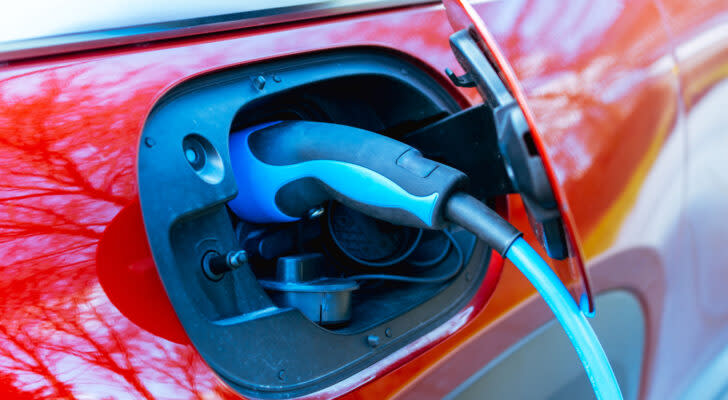 Closeup photo of red electric vehicle being charged with blue and black charger plugged into charging port. undervalued EV stocks.