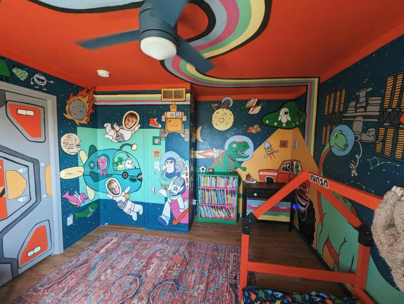 kids room with colorful space and dinosaur themed painted walls and ceiling