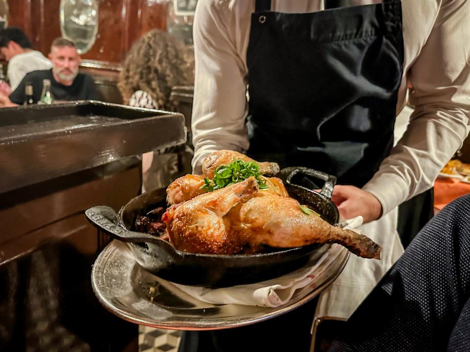 Roast chicken in cast-iron skillet on a silver tray being held by a server 