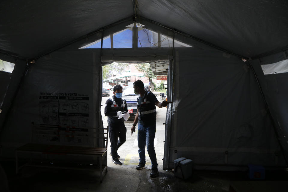 Arun Saiju, right, of the RNA-16 volunteer group, coordinates with teammate Rajesh Gaiju at a hospital in Bhaktapur, Nepal, Tuesday, May 26, 2020. RNA-16 stands for “Rescue and Awareness” and the 16 kinds of disasters they have prepared to deal with, from Nepal’s devastating 2015 earthquake to road accidents. But the unique services of this group of three men and a woman in signature blue vests in the epidemic amount to a much greater sacrifice, said doctors, hospital officials and civic leaders. (AP Photo/Niranjan Shrestha)