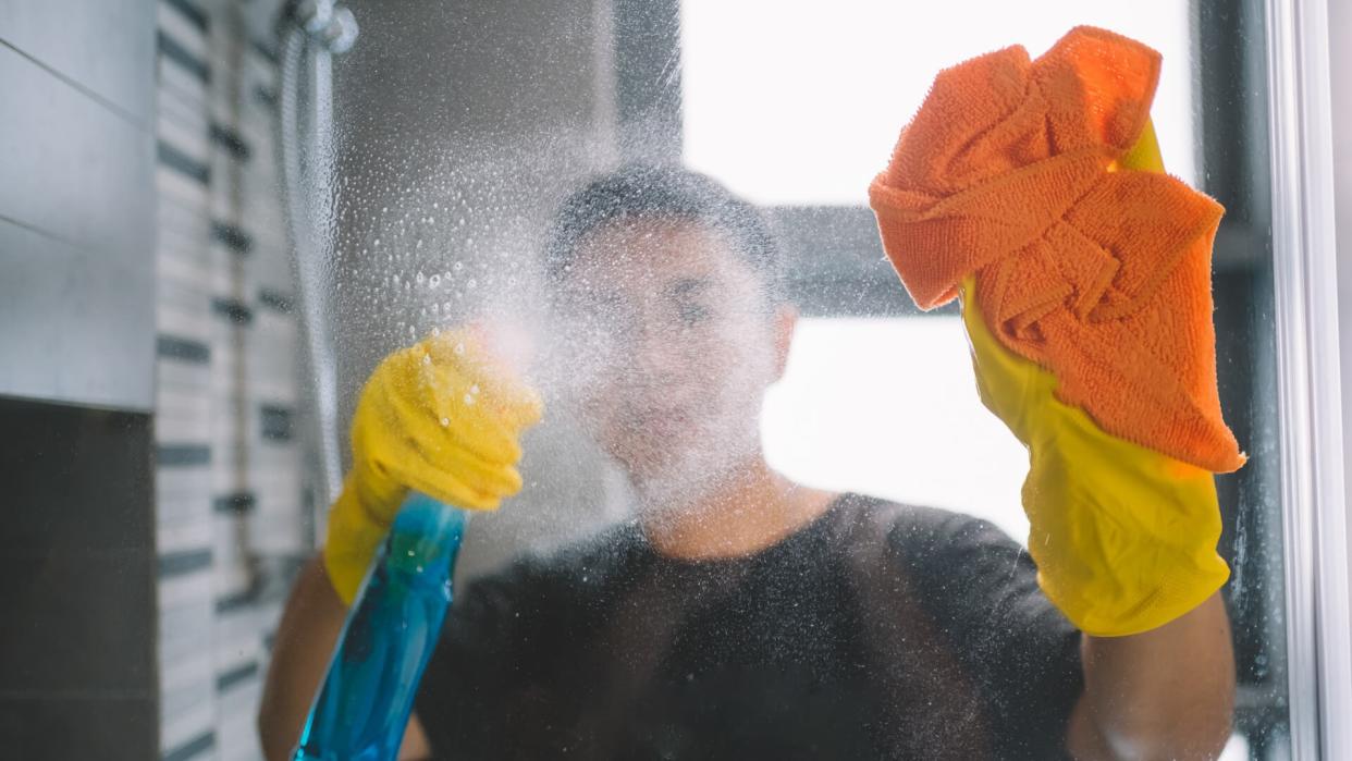 asian chinese male cleaning home with yellow gloves and orange colored cloth.
