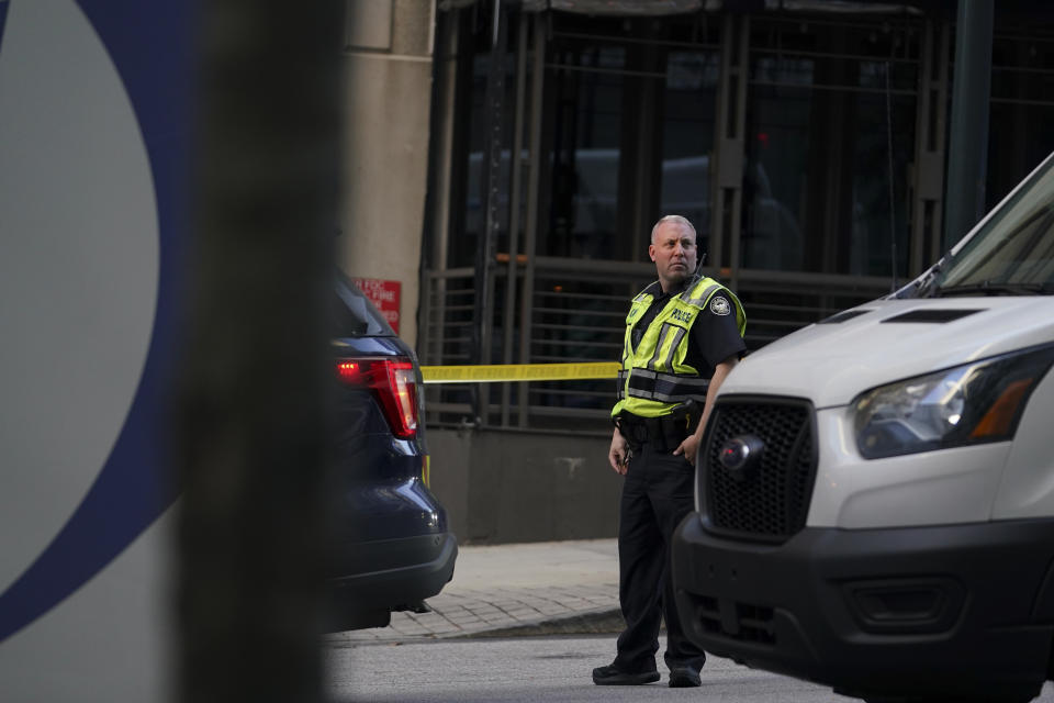 A police officer stands near the entrance of a residential building, Wednesday, Oct. 20, 2021, in Atlanta. Police in Atlanta have closed streets around at least four square blocks of office and apartment buildings in response to gunfire in the city's midtown area. (AP Photo/Brynn Anderson)