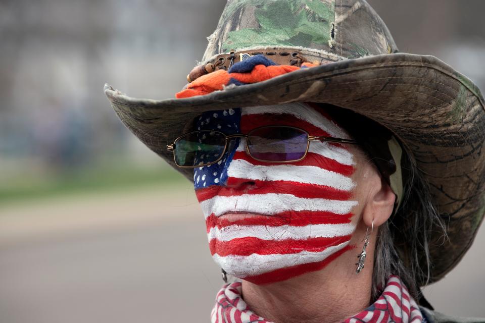 A woman with the US flag painted on her face gathers with others to protest coronavirus stay-at-home orders in Denver, Colorado.