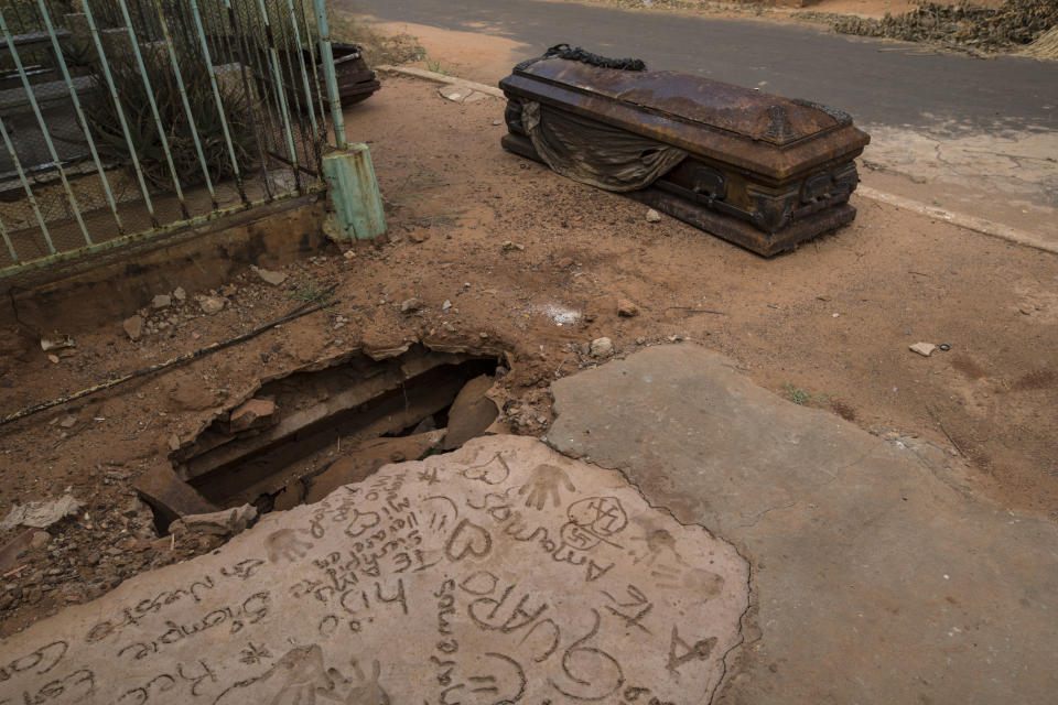 An oxidized coffin lies next to a grave that was dug up by thieves at "Corazon de Jesus" cemetery, or Heart of Jesus cemetery, in Maracaibo, Venezuela, Nov. 21, 2019. Thieves often raid graves for valuables, while public cemeteries often go abandoned, overgrown with weeds. (AP Photo/Rodrigo Abd)