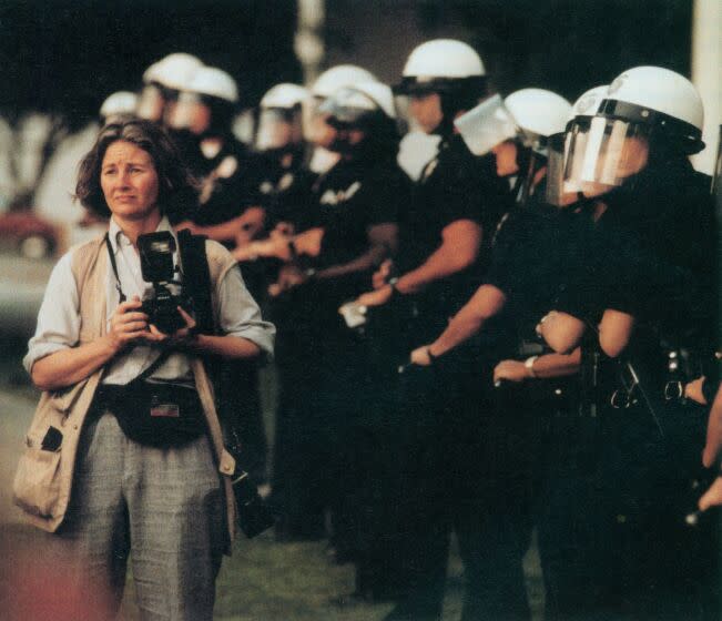 Los Angeles Times staff photographer Rosemary Kaul walks in front of police officers guarding Parker Center during the 1992 Los Angeles riots. This image was scanned from a special 1992 edition of Among Ourselves employee newsletter.