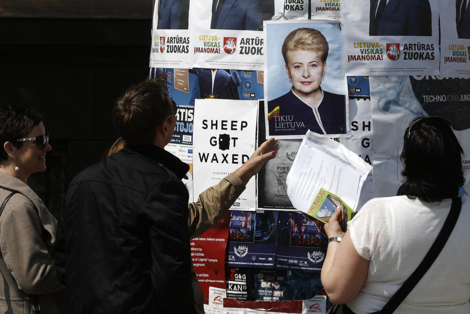 Local residents stand next to an election poster showing Lithuania's President Dalia Grybauskaite, a presidential candidate, installed in Vilnius, Lithuania, Friday, May 9, 2014. The poster reads "I believe in Lithuania". Lithuanians balloted Sunday, May 11, in a first round of presidential elections. (AP Photo / Mindaugas Kulbis)