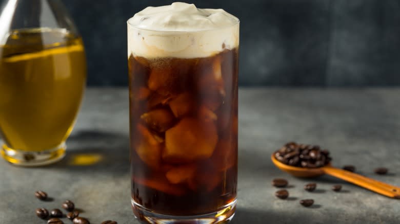 An iced olive oil coffee next to olive oil and coffee beans