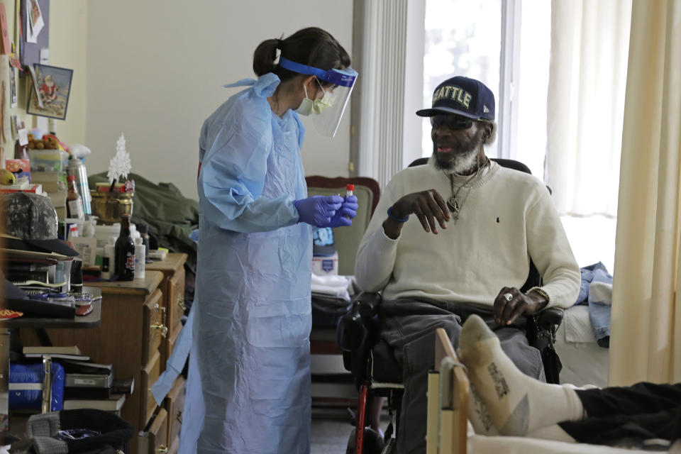 In this Friday, April 17, 2020, photo, Dr. Gabrielle Beger, left, prepares to take a nose-swab sample from Lawrence McGee, as she works with a team of University of Washington medical providers conducting testing for the new coronavirus at Queen Anne Healthcare, a skilled nursing and rehabilitation facility in Seattle. Sending "drop teams" from University of Washington Medicine to conduct universal testing at skilled nursing facilities in collaboration with public health officials is one aspect of the region's approach to controlling the spread of the coronavirus. (AP Photo/Ted S. Warren)