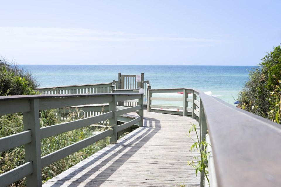 a low angle view down a wooden boardwalk leading to the beach and ocean in rosemary beach, florida