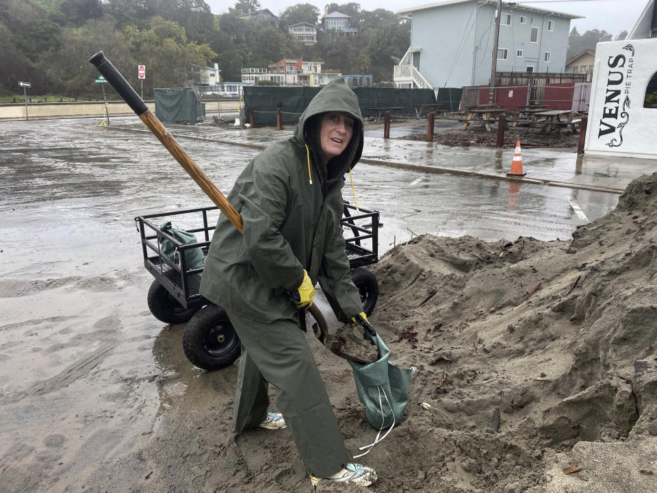 Resident Laurie Morse, 59, shovels wet sand into bags in the pouring rain, a last ditch effort to keep a rising creek out of her garage in the town of Rio Del Mar in Aptos, Calif., Wednesday, Jan. 11, 2023. Her roof was leaking, and along with her neighbors. The town has been dealing with every problem brought by the series of rainstorms rolling through California: massive logs and stumps are tumbling down the bloated Aptos Creek from the Santa Cruz mountains into the Monterey Bay, where high tides and large swells are tossing them back up the beach and into town. (AP Photo/Martha Mendoza)