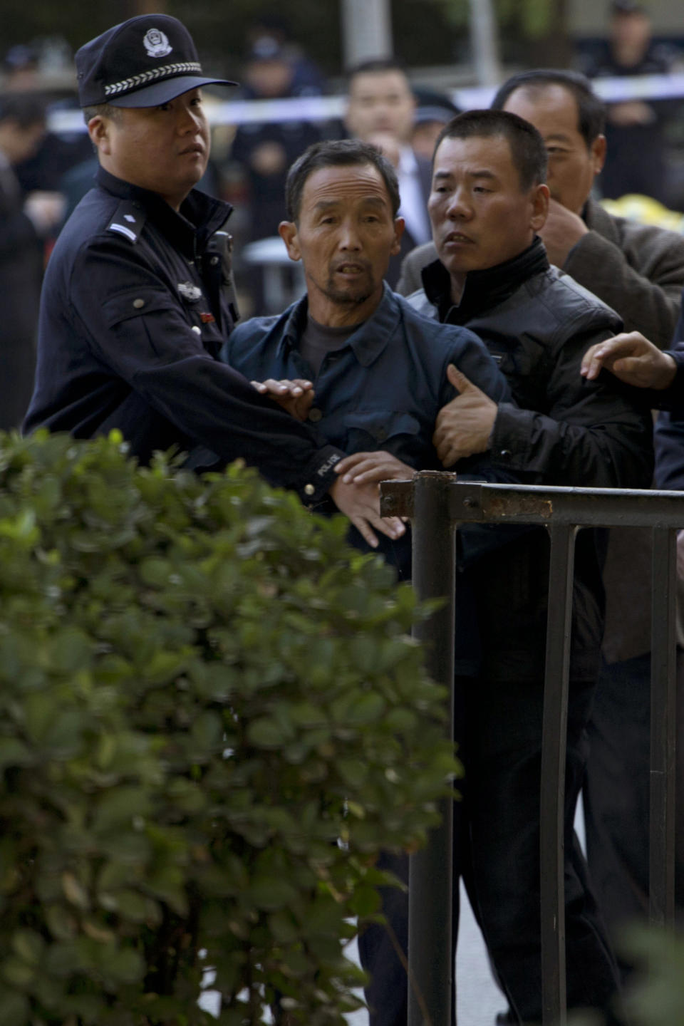 Ji Darong, center, the father of Beijing airport bomber Ji Zhongxing, is stopped by a Chinese police officer and plain clothes security personnel from approaching journalists gathered outside the Beijing Chaoyang District Court where Ji Zhongxing faced verdict and sentencing in Beijing, China, Tuesday, Oct. 15, 2013. Ji Zhongxing, a partly paralyzed man who exploded a bomb inside Beijing's airport in hopes of winning redress over an alleged beating by public officials, was given a six-year prison sentence Tuesday. (AP Photo/Ng Han Guan)