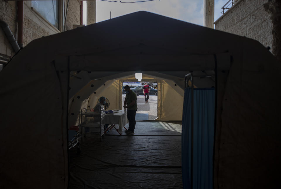 A Palestinian medic checks a person's temperature to screen for coronavirus symptoms, inside a temporary tent at the entrance al-Quds Hospital, in Gaza City, Monday, Sept. 7, 2020. Dozens of front-line health care workers have been infected, dealing a new blow to overburdened hospitals. (AP Photo/Khalil Hamra)