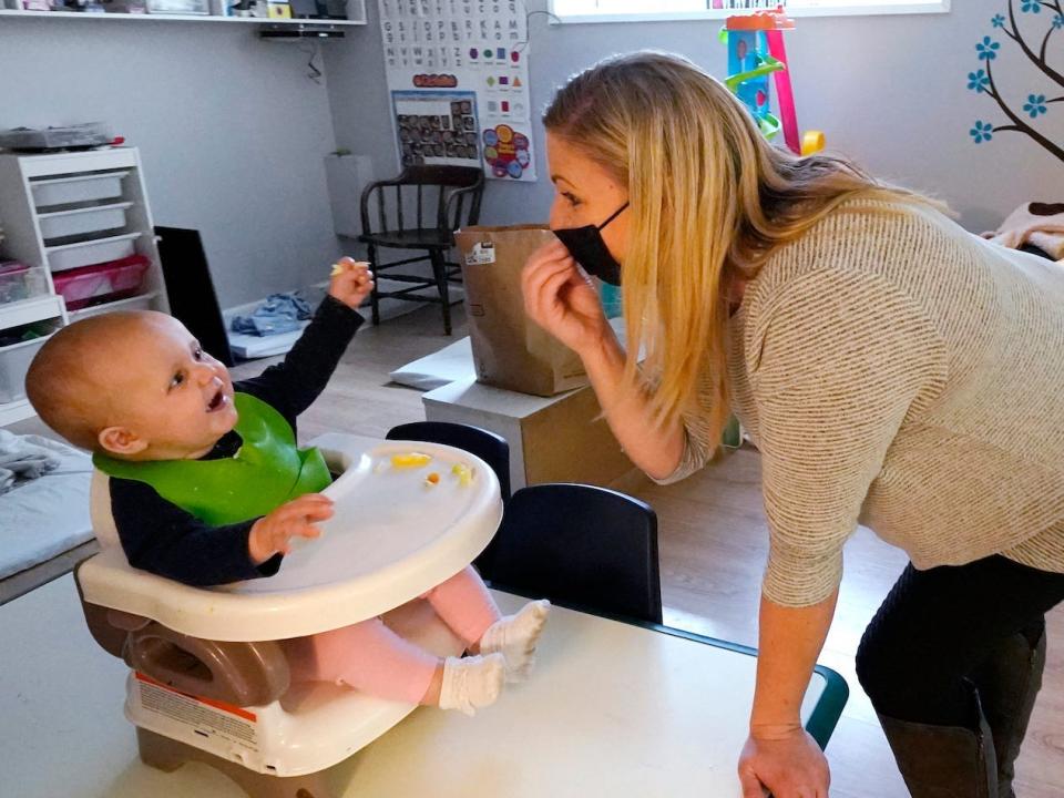 woman with a mask on signing about eating food to baby in a high chair