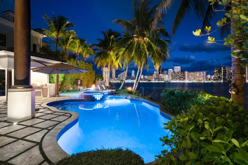 A stunning view of the pool at night, with city skyline and water views. Become Legendary / ONE Sotheby's International Realty