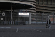 Two people walk by a notice outside San Siro stadium advising that the Serie A soccer match between Inter and Sampdoria is cancelled, in Milan, Italy, Sunday, Feb. 23, 2020. In Lombardy, the hardest-hit region by the spread of the Coronavirus with 90 cases, schools and universities were ordered to stay closed in the coming days, and sporting events were canceled. Lombardy's ban on public events also extended to Masses in churches in the predominantly Roman Catholic nation. (AP Photo/Antonio Calanni)