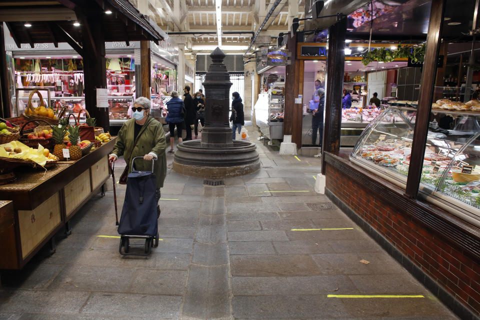 An elderly woman wears a face mask as she shops in an indoor food market, in Paris, Tuesday, May 12, 2020. Food markets reopened in Paris on Tuesday as France is cautiously easing the two-month lockdown across the country. Specific measures, such as more widely spaced stalls, have been implemented to enforce physical distancing. (AP Photo/Thibault Camus)