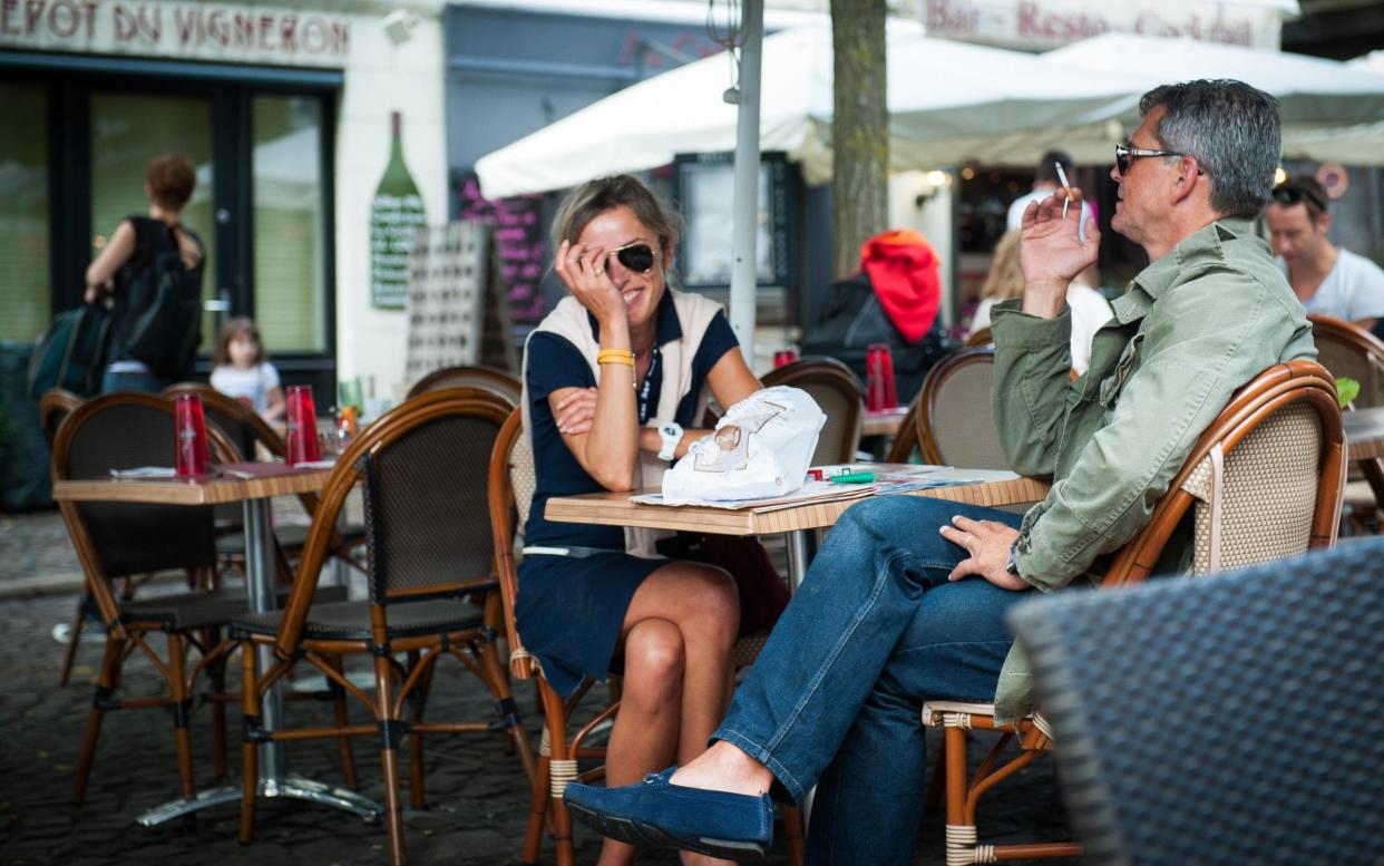 A couple smoke at a table outside a cafe in France