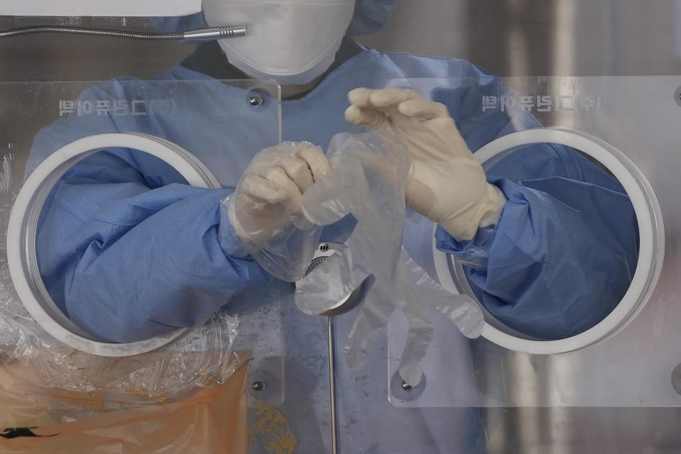 A medical worker wearing protective gear in a booth, wears plastic gloves at a temporary screening clinic for the coronavirus in Seoul, South Korea, Monday, Nov. 29, 2021. (AP Photo/Lee Jin-man)