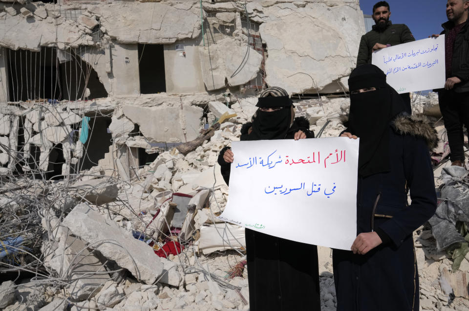 FILE - Women stand amidst the rubble of destroyed houses with placards in Arabic reading "United Nations are the partners of Bashar Assad and killing Syrians," in Atareb, Syria, Sunday, Feb. 12, 2023. The massive earthquake that hit last week is the latest in a litany of hardships for Syrian women, many of whom have been left dependent on aid and alone responsible for their families' well-being. (AP Photo/Hussein Malla, File)